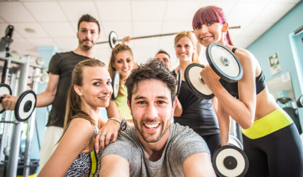 Group of sportive people in a gym taking selfie - Happy sporty friends in a weight room while training - Concepts about lifestyle and sport in a fitness club